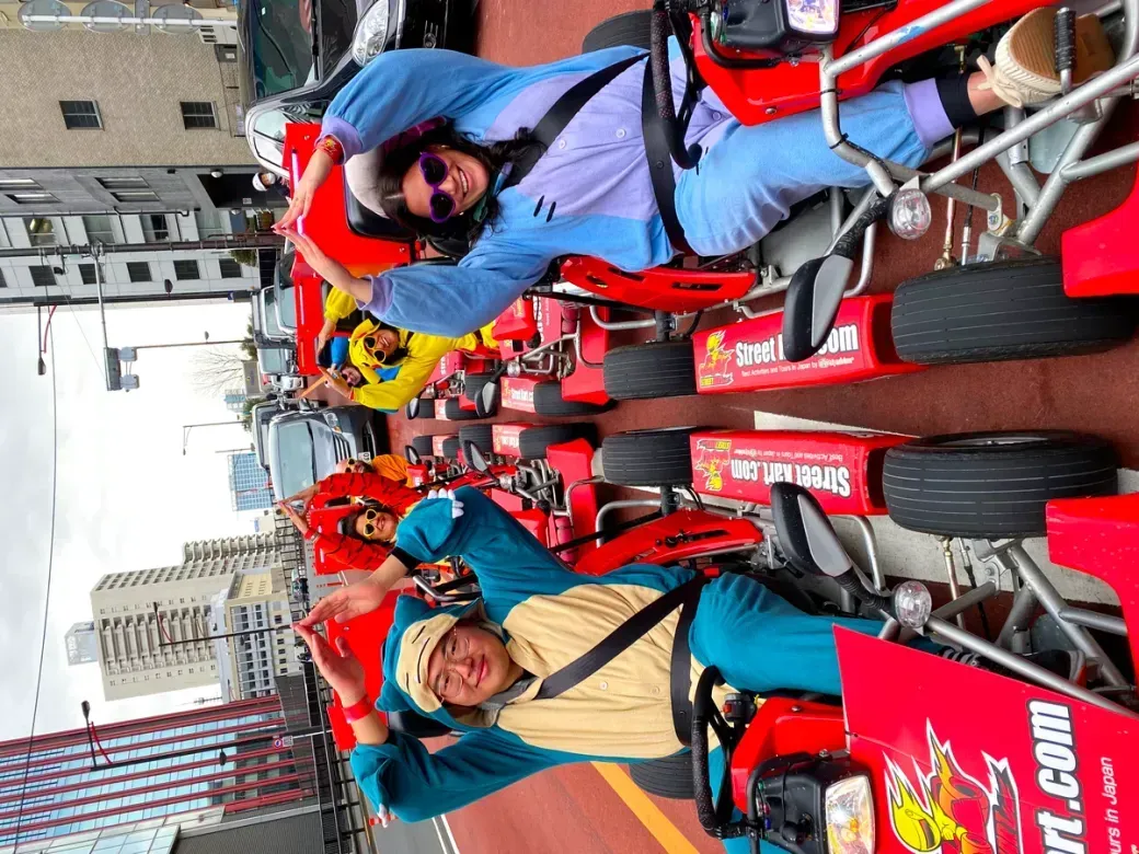 Group of people in red go-karts on a city street, waving and smiling at the camera.