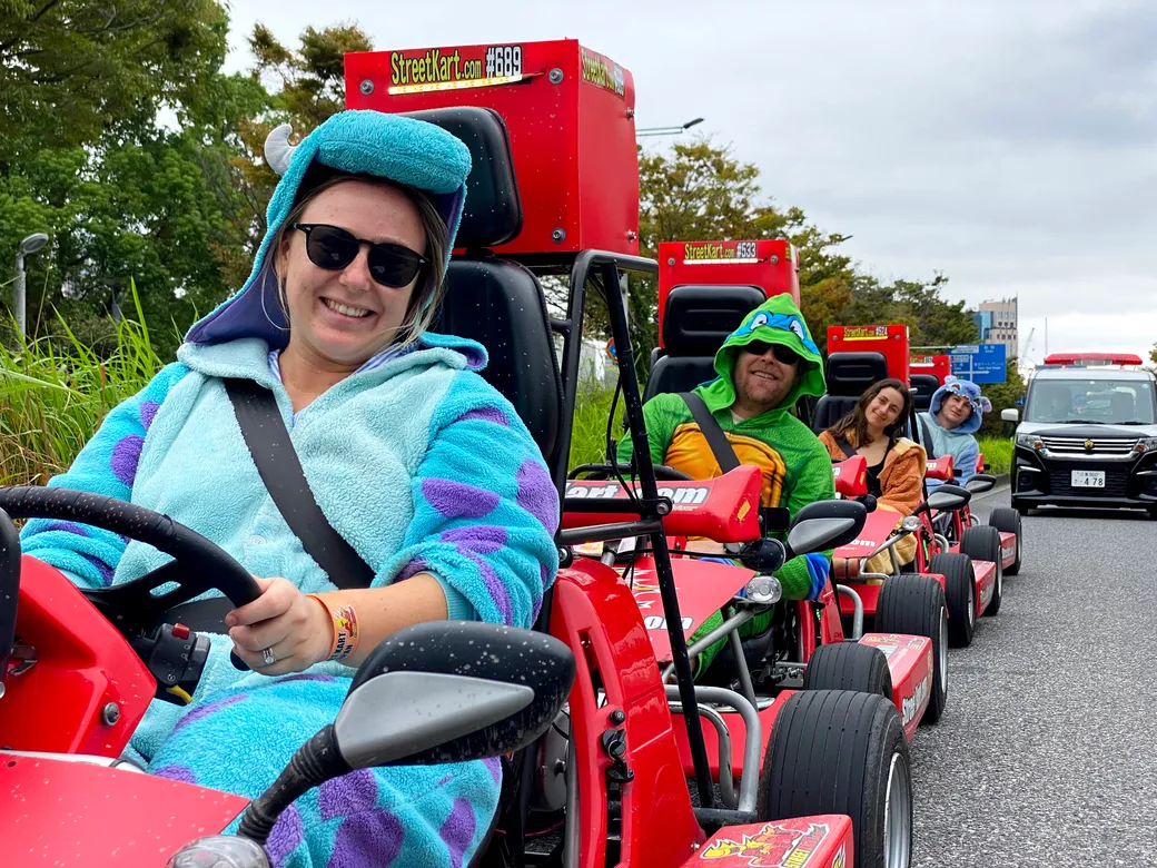Front driver in sunglasses wearing a blue turtle-costume, steering a red StreetKart go-kart in a parade line